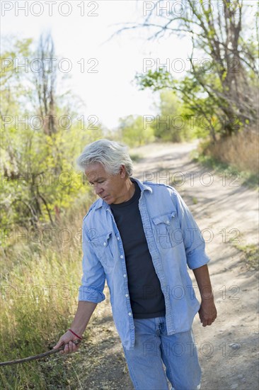 Caucasian man walking on dirt road holding stick