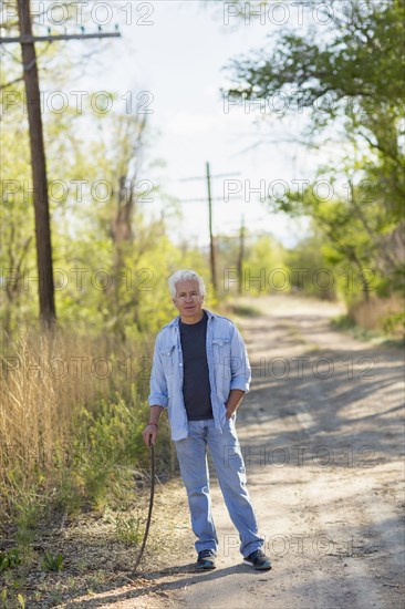 Caucasian man standing on dirt road holding stick