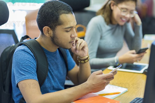 Mixed Race boy and girl texting on cell phones in library