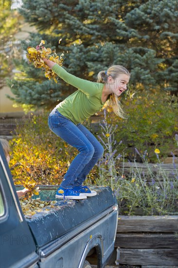 Caucasian girl holding autumn leaves jumping off truck