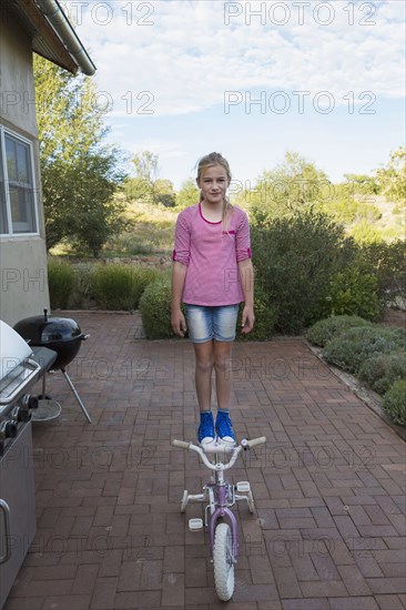 Caucasian girl standing on seat of bicycle