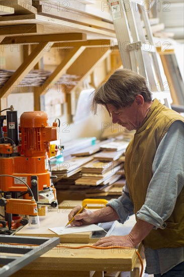 Caucasian carpenter writing on notepad in workshop