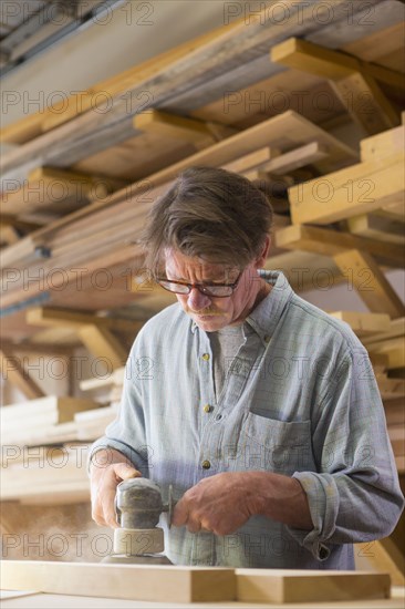 Caucasian carpenter sanding wood in workshop