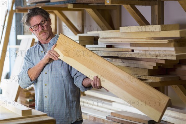 Caucasian carpenter eyeballing wooden plank in workshop