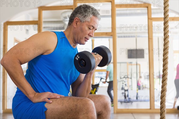 Mixed Race man curling dumbbell in gymnasium