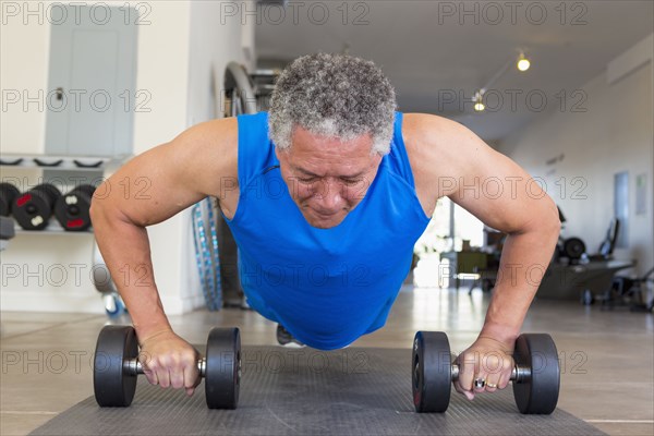 Mixed Race man doing push-ups with dumbbells in gymnasium