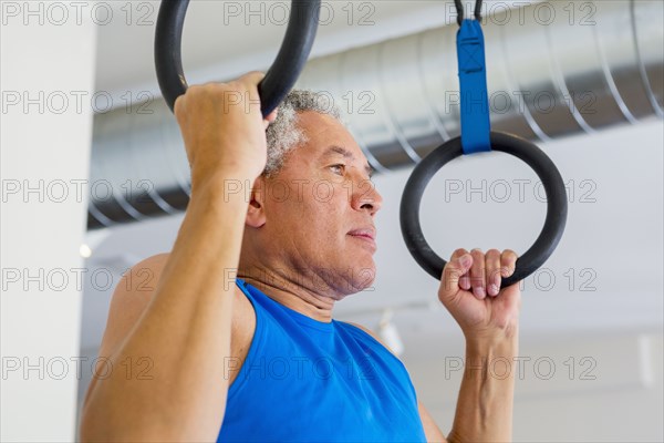 Mixed Race man using pull-up rings in gymnasium