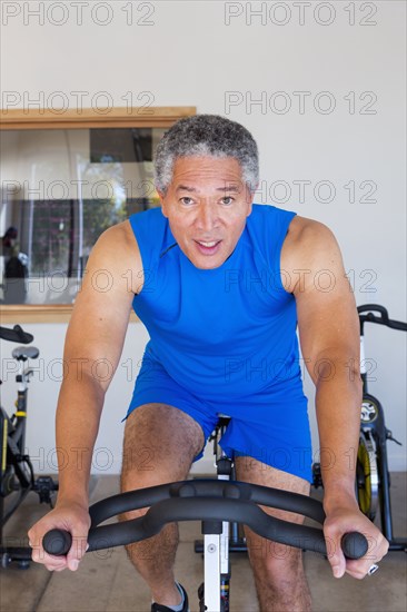 Mixed Race man riding stationary bicycle in gymnasium