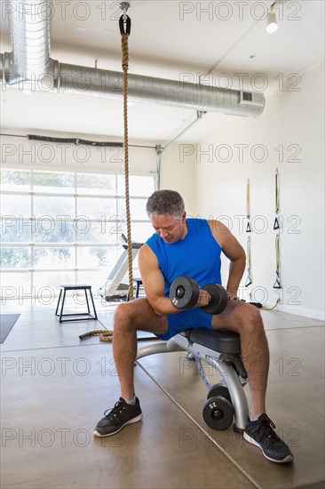 Mixed Race man curling dumbbell in gymnasium