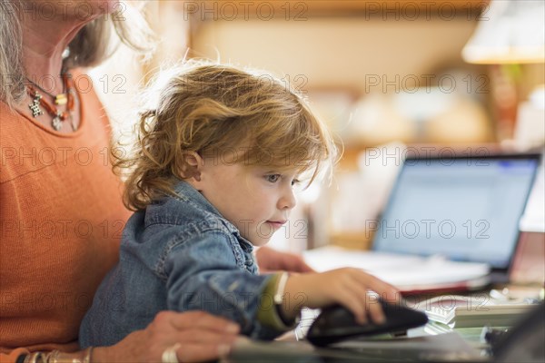 Caucasian baby boy in lap of grandmother using computer mouse