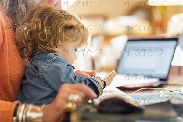 Caucasian baby boy in lap of grandmother using computer keyboard