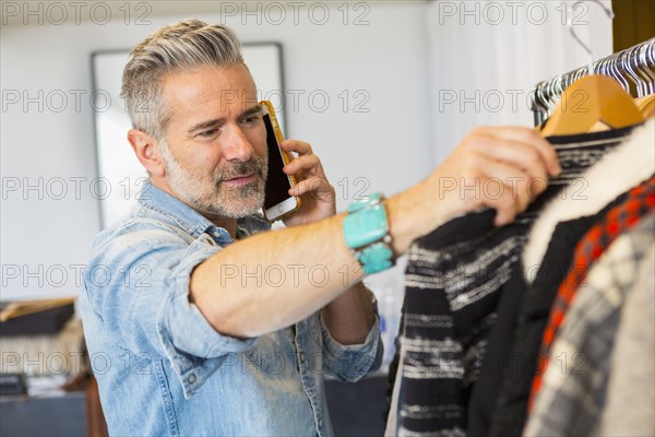 Caucasian man talking on cell phone examining clothing