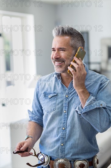 Caucasian man holding eyeglasses talking on cell phone