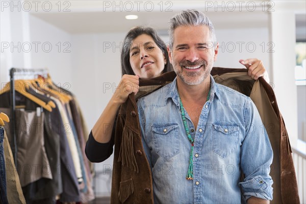 Woman helping man with fringe jacket in store