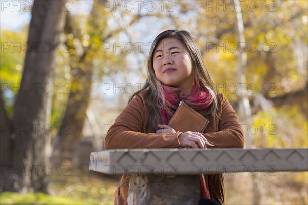 Asian woman holding journal at table in autumn