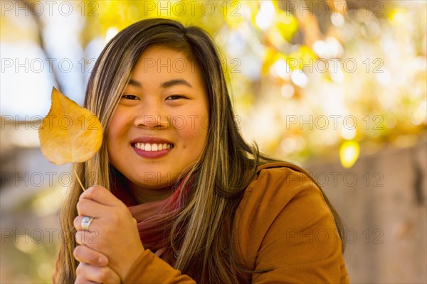 Smiling Asian woman holding leaf in autumn