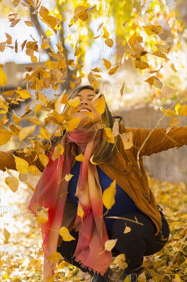 Smiling Asian woman throwing leaves in autumn
