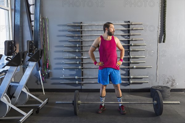 Mixed Race man resting near barbell in gymnasium