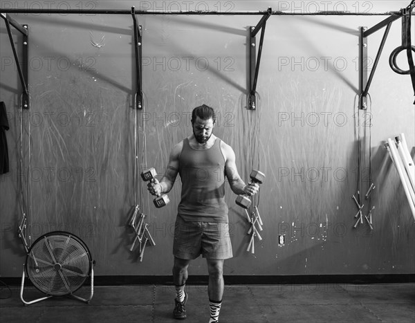 Mixed Race man lifting dumbbells in gymnasium