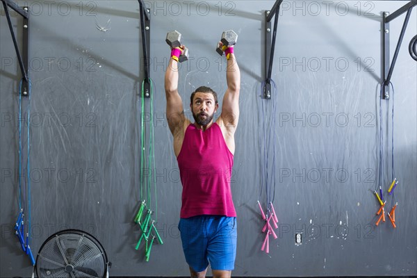 Mixed Race man lifting dumbbells in gymnasium