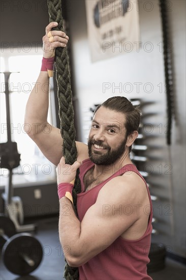 Mixed Race man climbing rope gymnasium