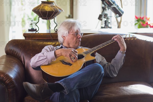 Caucasian man playing guitar on sofa