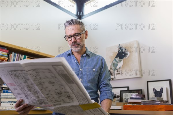 Caucasian man reading blueprint in office