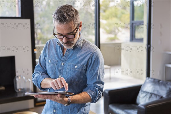 Caucasian man standing in livingroom using digital tablet