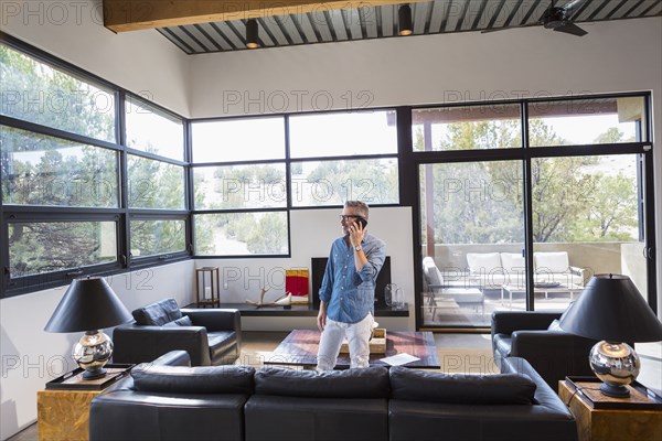 Caucasian man standing in livingroom talking on cell phone