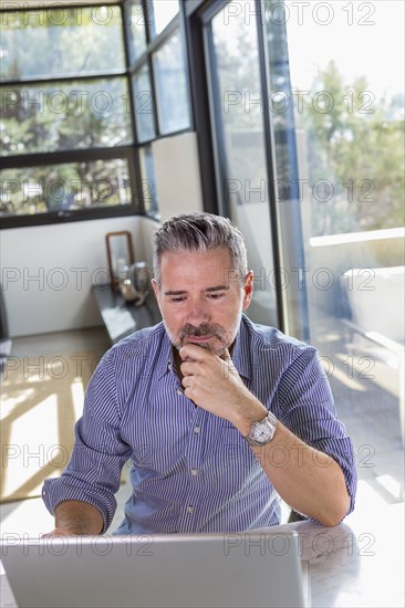 Pensive Caucasian man sitting at table using laptop