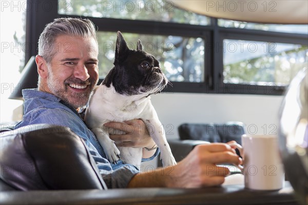 Caucasian man hugging dog on sofa and drinking coffee