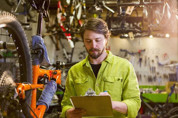 Caucasian worker writing on clipboard in bicycle shop