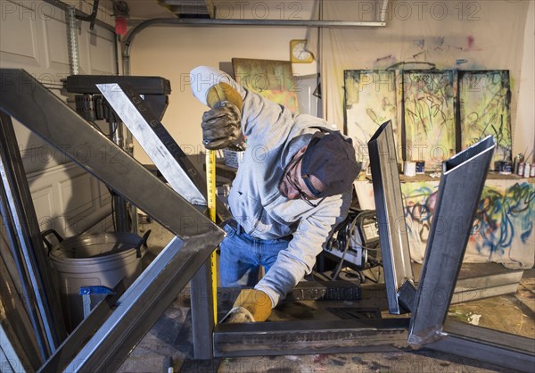 Caucasian man measuring metal sculpture with tape measure