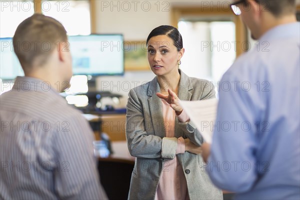 Businesswoman gesturing and talking to businessmen in office