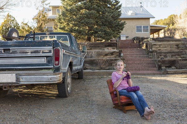 Caucasian girl sitting on chair near truck and knitting