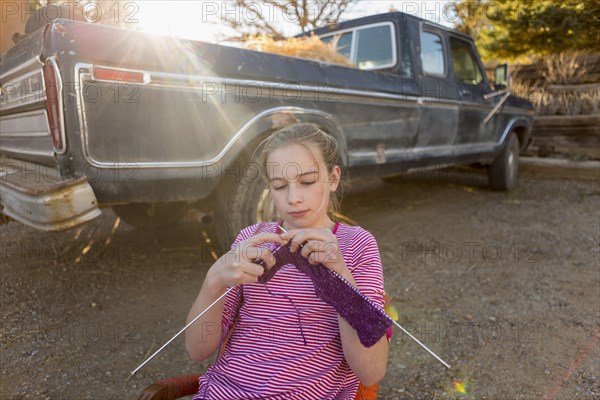 Caucasian girl sitting on chair near truck and knitting