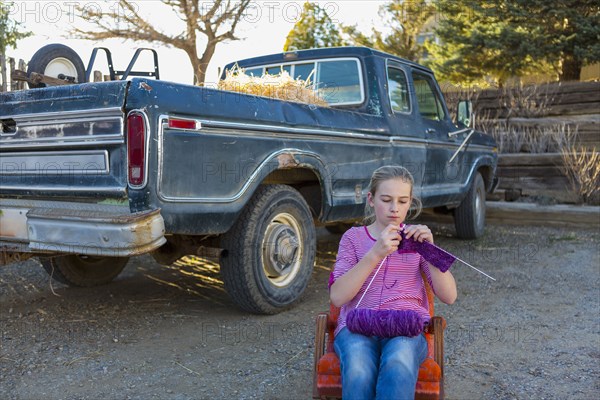 Caucasian girl sitting on chair near truck and knitting