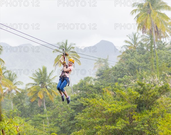 Caucasian girl hanging on zip line in forest