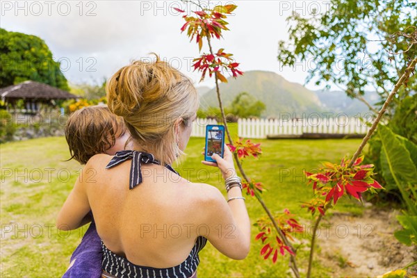 Caucasian mother carrying son and photographing with cell phone