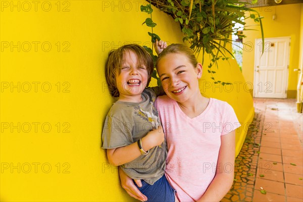 Caucasian girl leaning on yellow wall holding brother