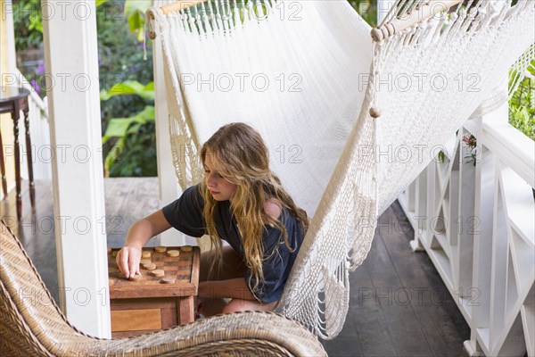 Caucasian girl sitting in hammock playing checkers