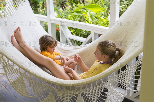 Caucasian brother and sister laying in hammock eating snack