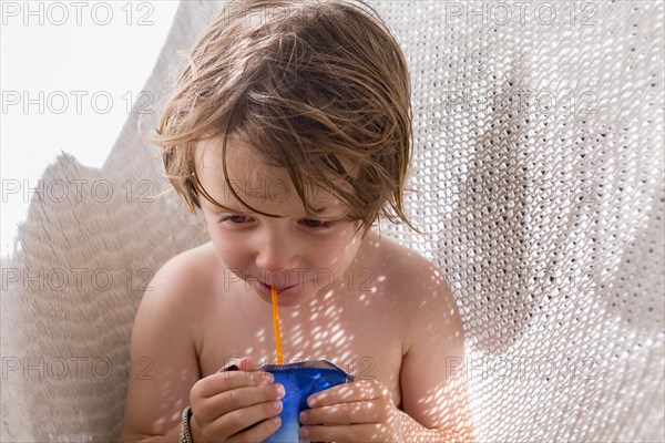 Caucasian boy drinking juice through straw in hammock