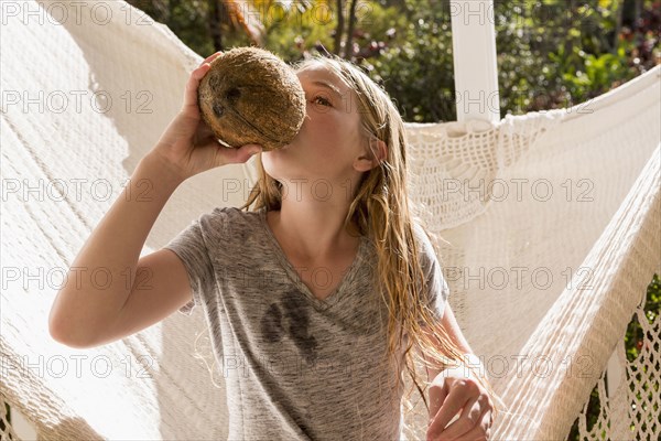 Caucasian girl sitting in hammock drinking from coconut