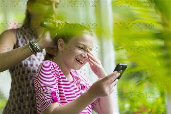 Caucasian mother brushing hair of daughter texting on cell phone