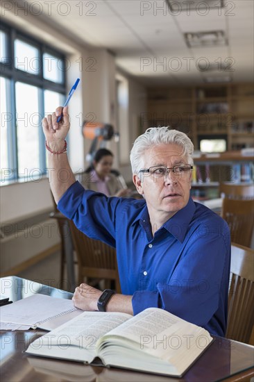 Older man in library raising hand and asking question