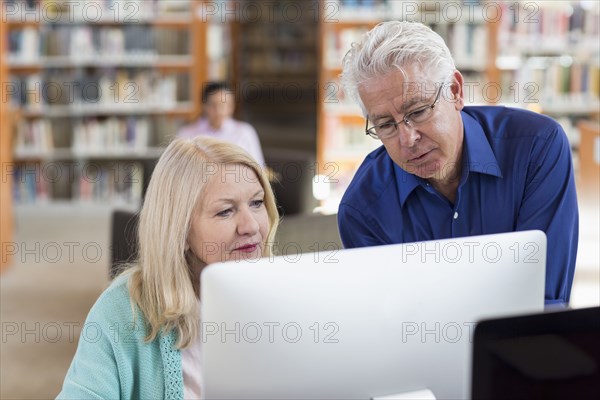 Older man helping woman using computer in library