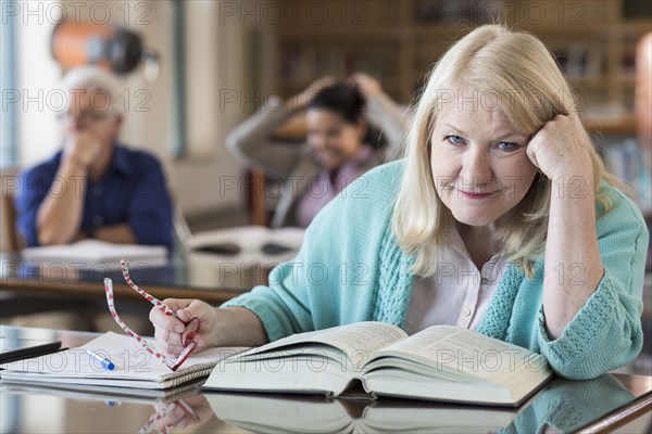 Confused older woman reading book in library