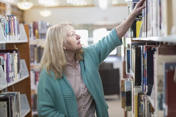 Curious Caucasian woman reaching for book in library