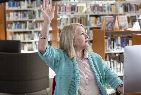 Caucasian woman using computer in library raising hand